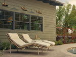 Two Neighbor Camber Chaise Lounges with cream cushions and woven cord backs reclined on a brick paver patio beside a sunken hot tub.