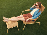 Woman relaxing outdoors on Neighbor Hopper Chair and Ottoman in sand finish on grass, lifestyle product image