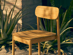 Neighbor Keeper Dining Chairs in natural teak with woven details in garden setting with potted plants and stone wall