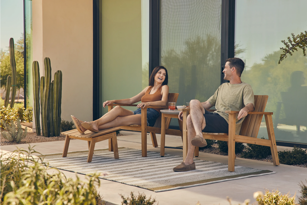 Neighbor Low Chairs in Sand color positioned on modern patio with glass wall backdrop, minimalist cast aluminum design, contemporary setting