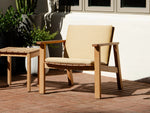 Neighbor Low Chair with beige cushion pad on wood deck patio beside potted plants, teak frame minimalist Adirondack design