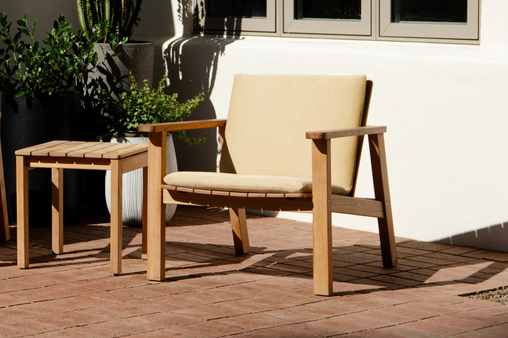 Neighbor Low Chair with beige cushion pad on wood deck patio beside potted plants, teak frame minimalist Adirondack design