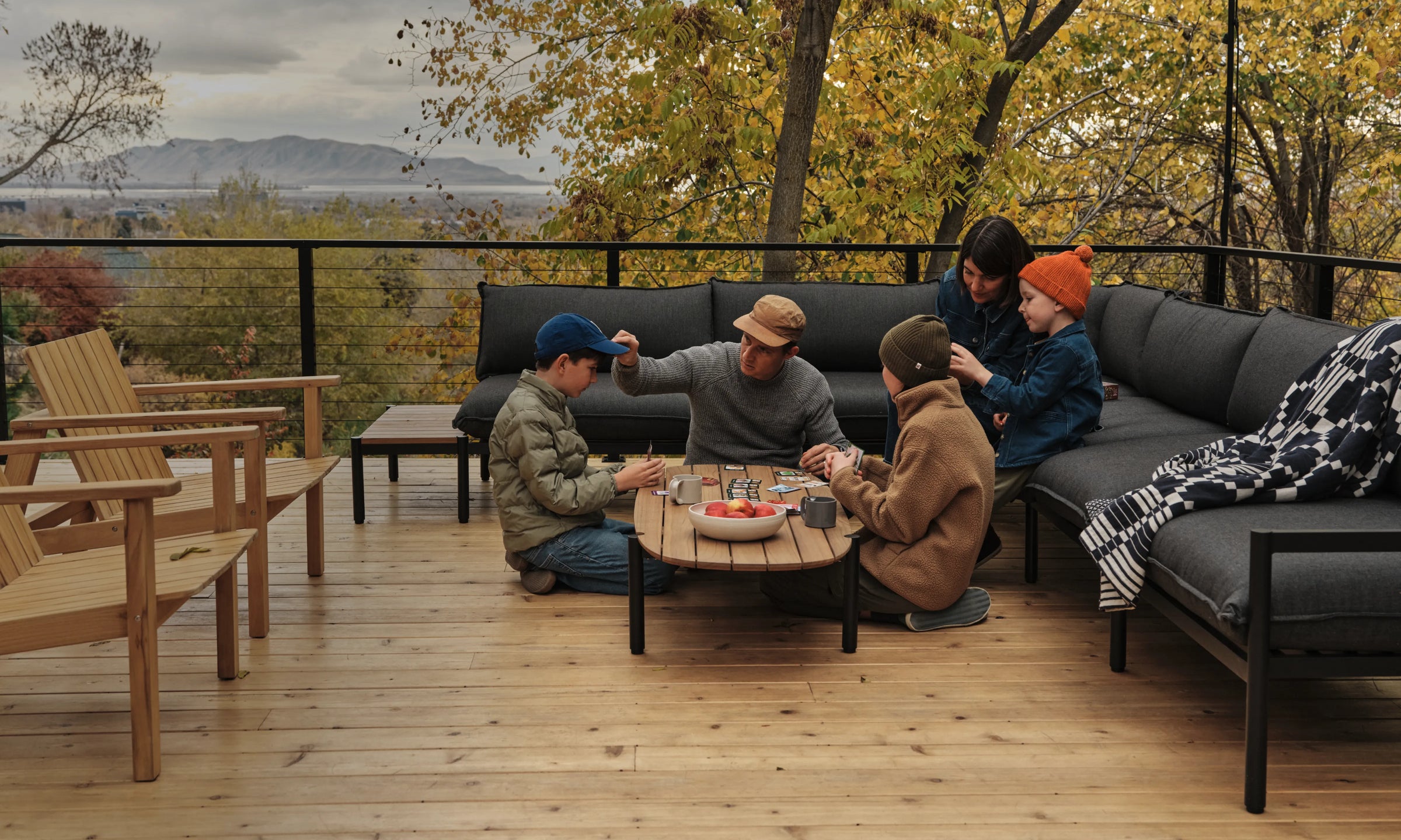 Jones Family sitting on their Terra Sectional while playing a card game on the Terra Coffee Table on their deck with fall foliage in the background.