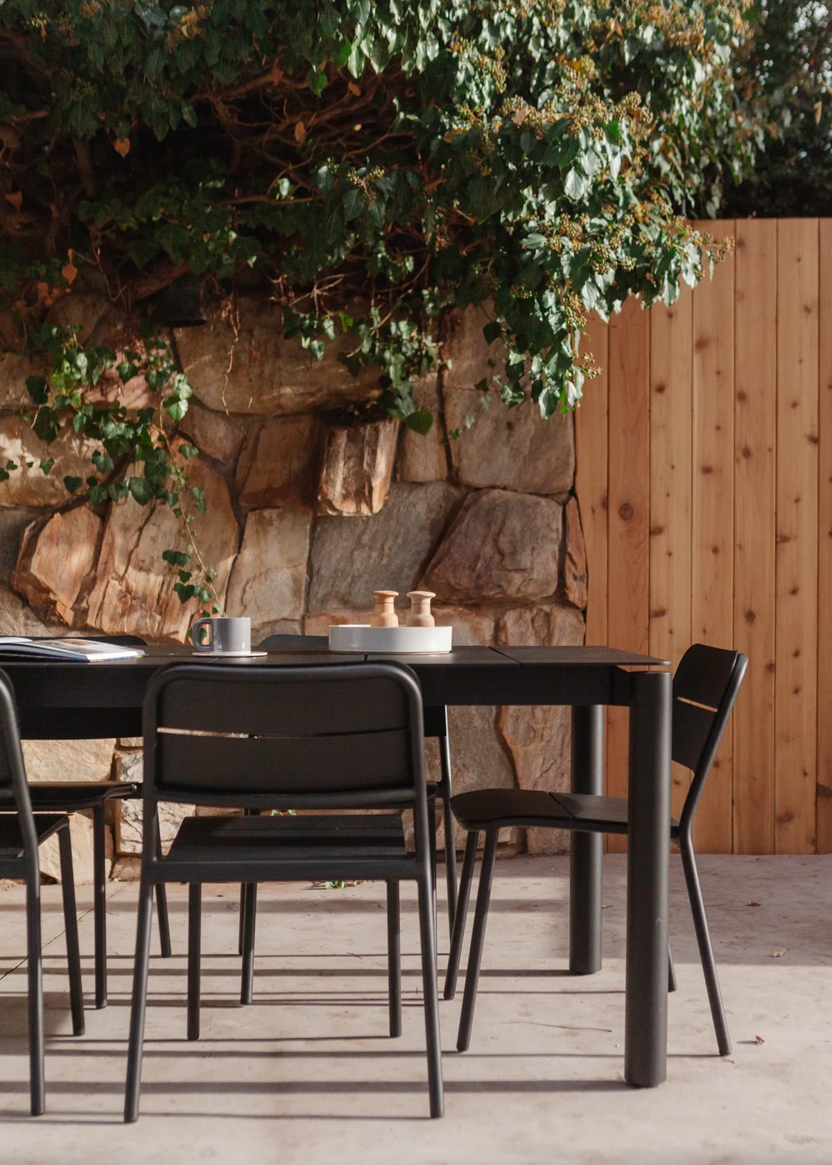 Neighbor Bandwidth Dining Set placed outside with tree and wooden fencing. 