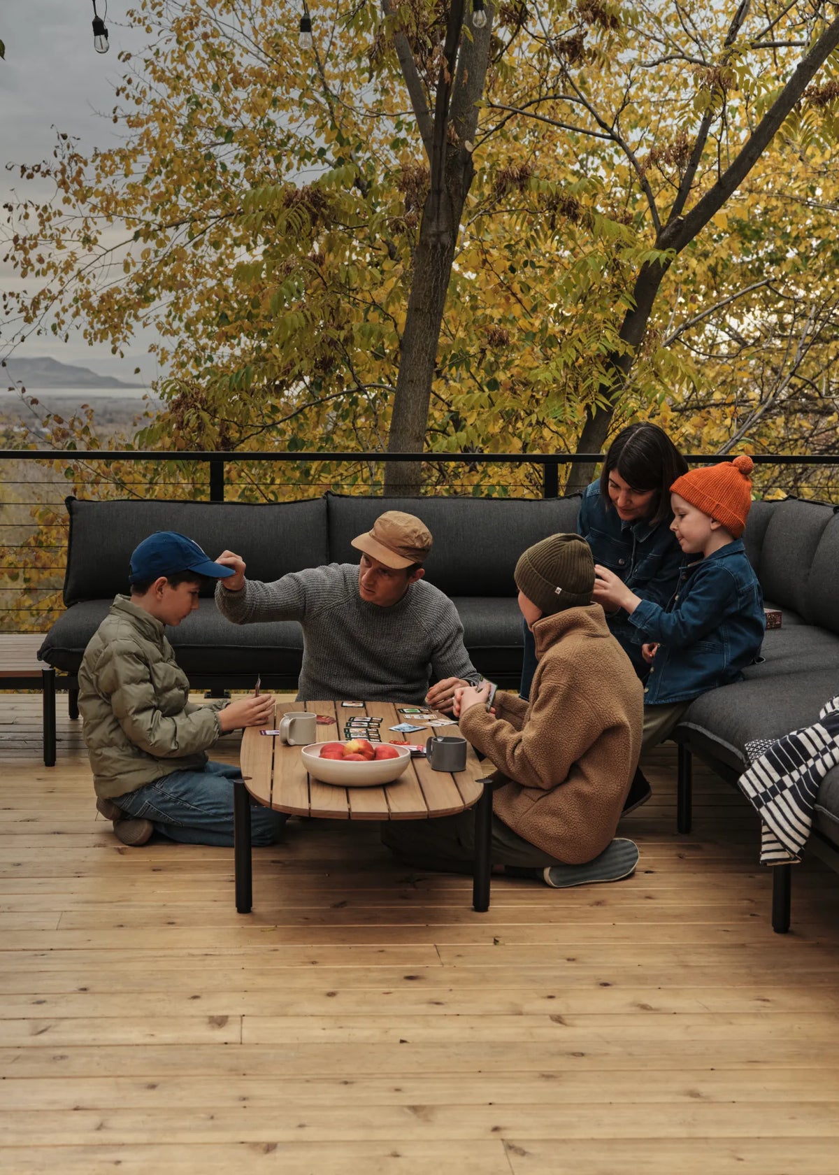 Jones Family sitting on their Terra Sectional while playing a card game on the Terra Coffee Table on their deck with fall foliage in the background.