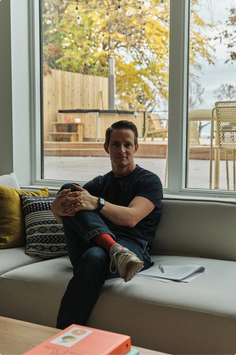 Cree Jones sitting on an indoor bench by a window, hands clasped over his knees