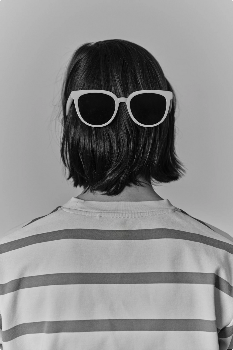 A child seen from behind with sunglasses pushed up on their head, wearing a striped shirt