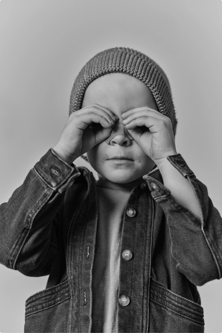 A child in a knit beanie covering their eyes with their hands in a playful gesture