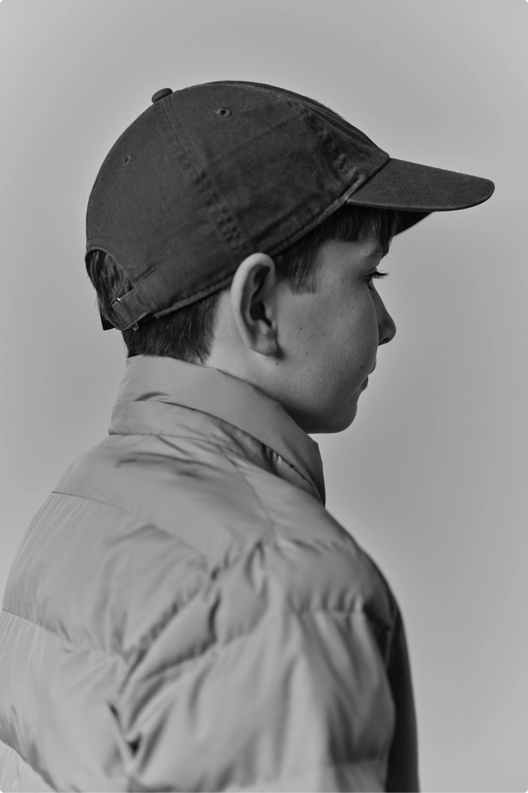 A child in a baseball cap and puffy jacket looking off to the side