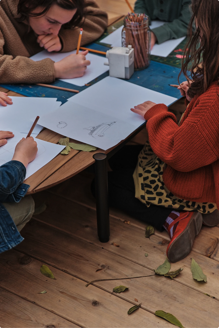 Two children drawing on paper spread across the wood deck floor