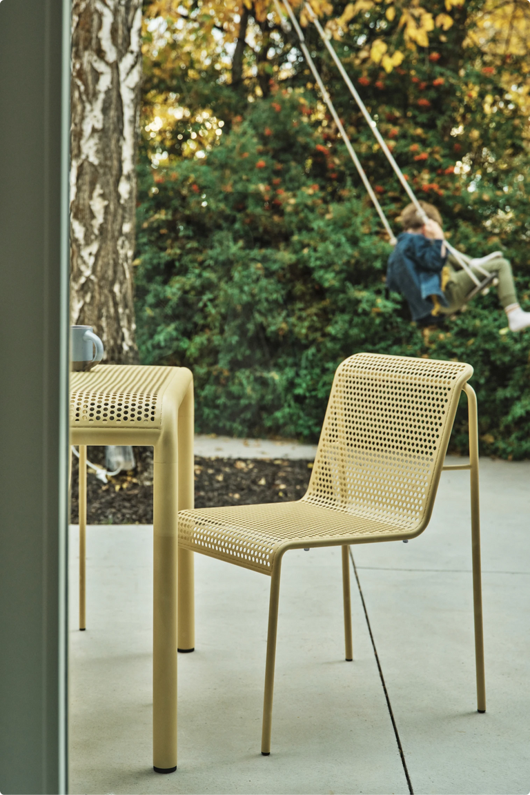 A yellow perforated Neighbor outdoor chair, with a child swinging in the background