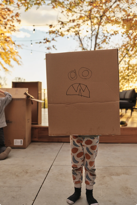 A child wearing a cardboard box decorated like a robot face over their head