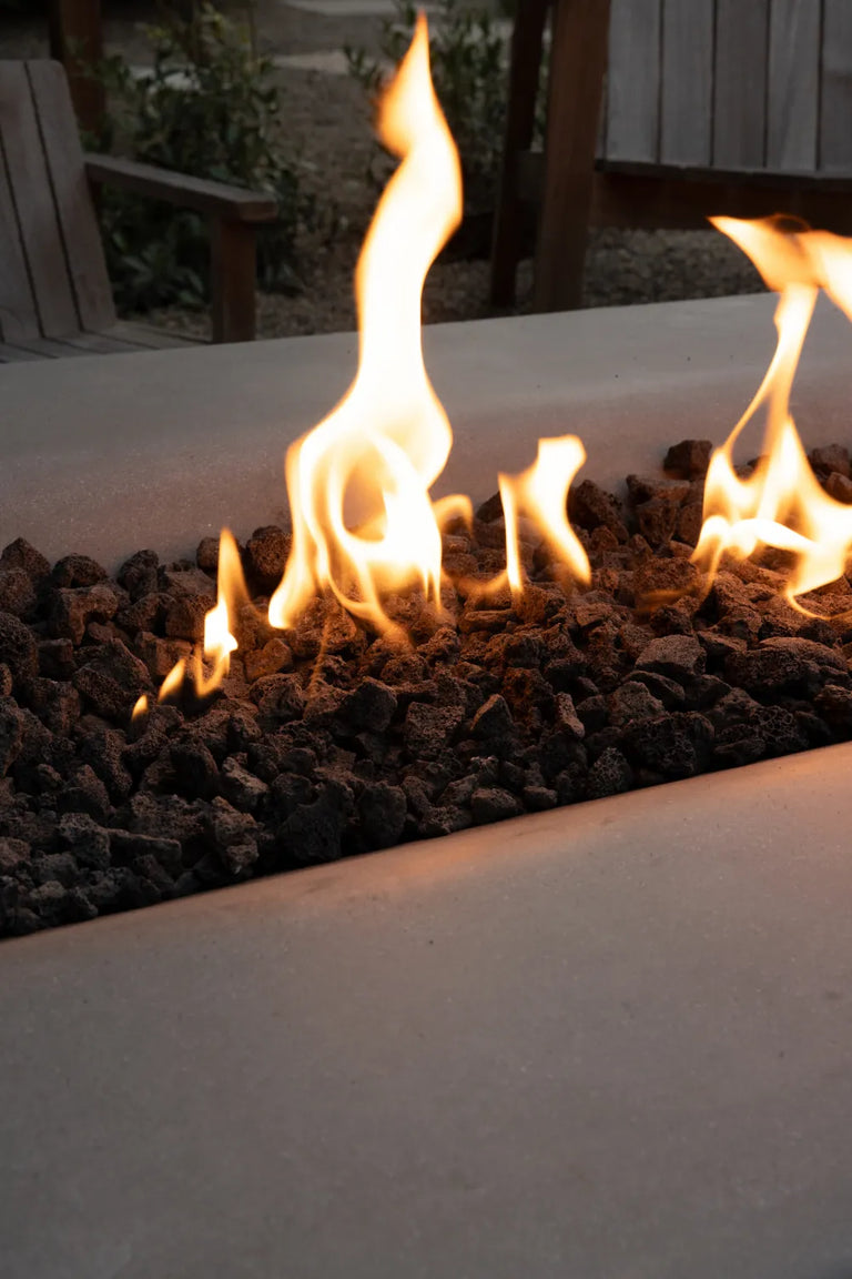Close-up of flames rising from lava rock inside a Rook Fire Table, with wooden chairs blurred in the background