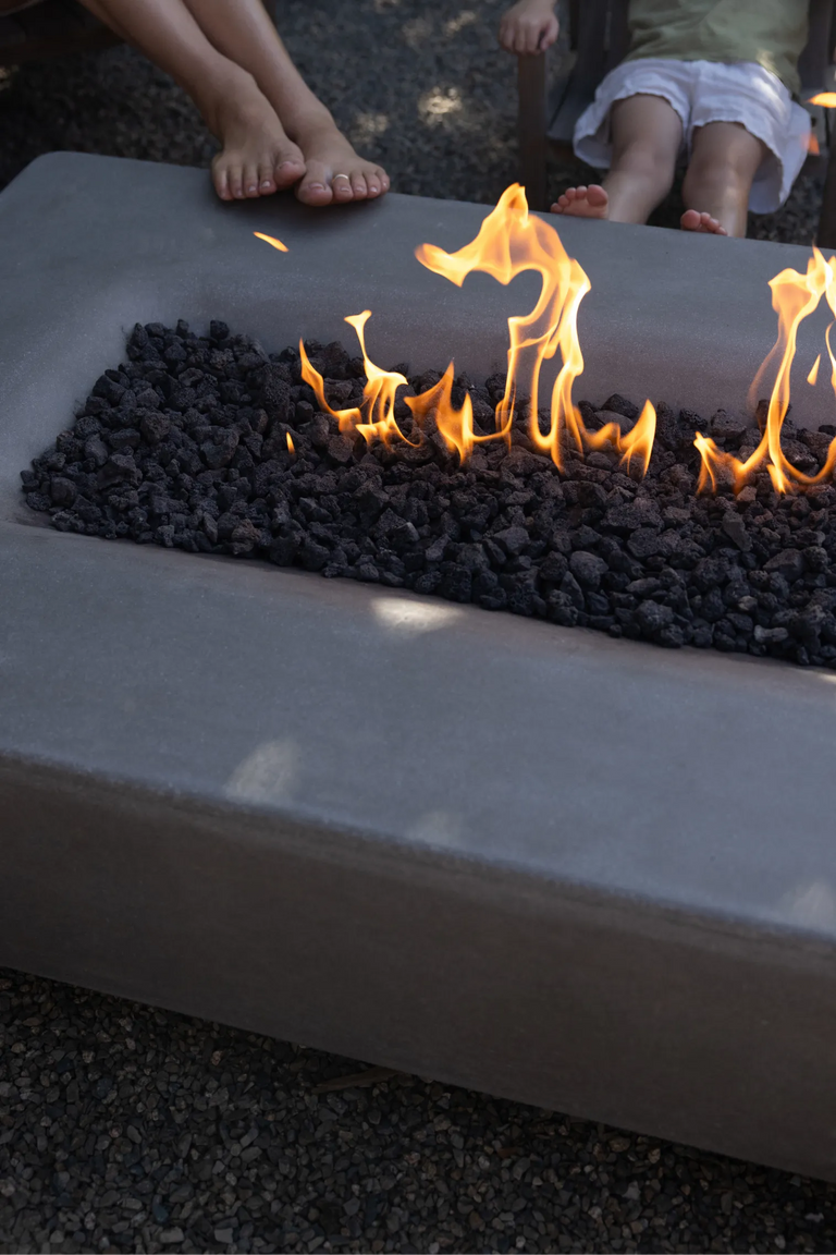Two children's bare feet propped on the edge of a lit Rook Fire Table