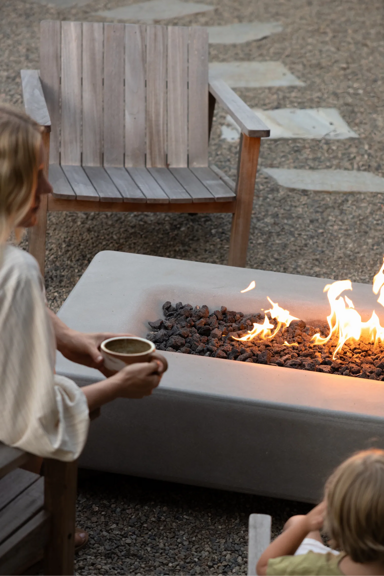 Taylr Anne Castro holds a mug of matcha while sitting beside the fire table, with her son nearby