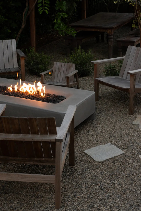 Wooden chairs arranged around a lit Rook Fire Table at dusk