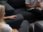 Neighbor Roundabout Sectional with wicker weave and white cushions arranged on residential patio near glass doors