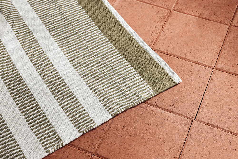 Neighbor Dune Rug in Basil with horizontal stripes in sage and white on terracotta tile patio surface