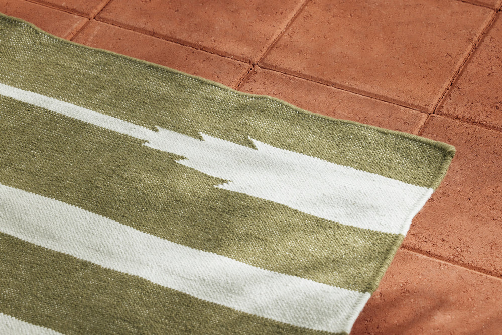 Neighbor Mesa Rug in Basil with olive and cream striped geometric pattern on terracotta tile patio surface