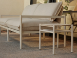 Neighbor Underline Side Table in off-white, a compact two-tier table on slim tubular legs, next to a cushioned sofa.