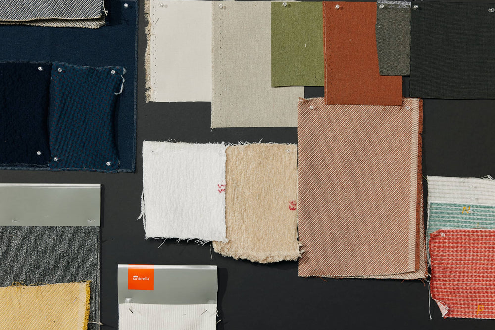 Fabric swatches in navy, cream, rust, olive, and striped patterns pinned to a dark board with a Sunbrella swatch card