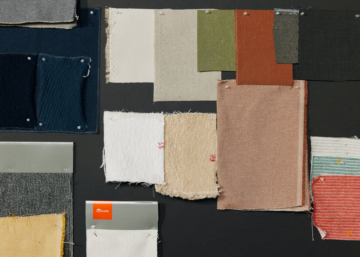 Fabric swatches in navy, cream, rust, olive, and striped patterns pinned to a dark board with a Sunbrella swatch card