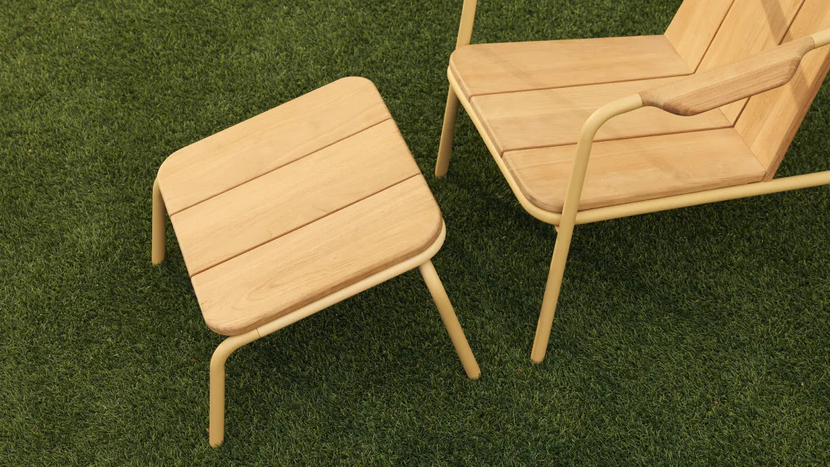 Close detail shot of a Neighbor Hopper Ottoman with natural-wood slat top and yellow powder-coated tubular steel frame placed on artificial-turf grass beside the matching Neighbor Hopper Chair, showing the seamless visual pairing of the two pieces.