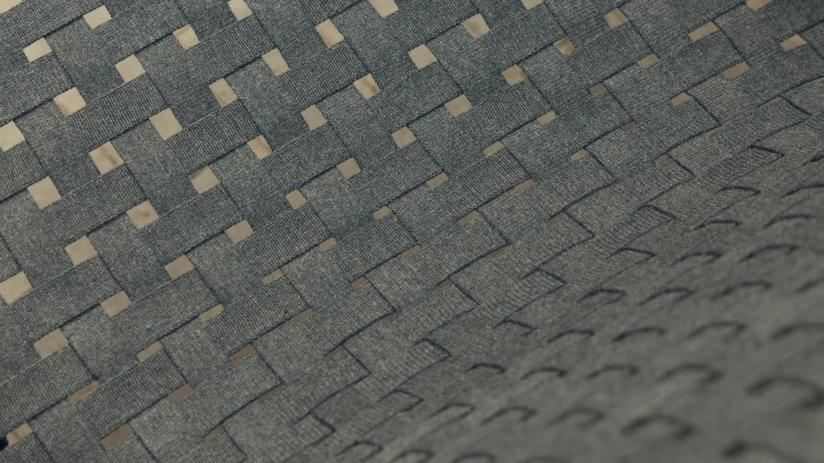 Extreme close-up macro of the Neighbor Up-Down Chair's charcoal woven-strap seat showing the herringbone-style basket weave, with subtle natural-tone fibers peeking through the dense grid pattern.