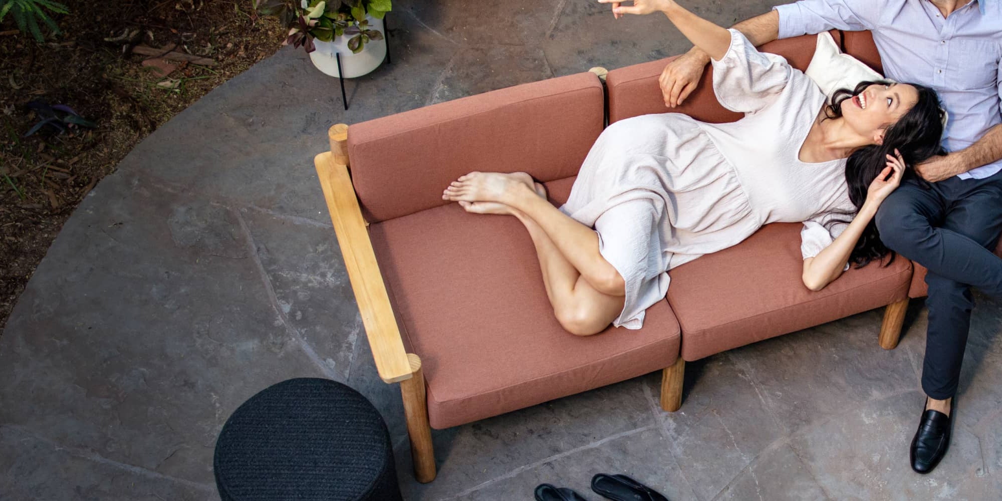 Couple comfortably laying on rust-colored outdoor sofa together