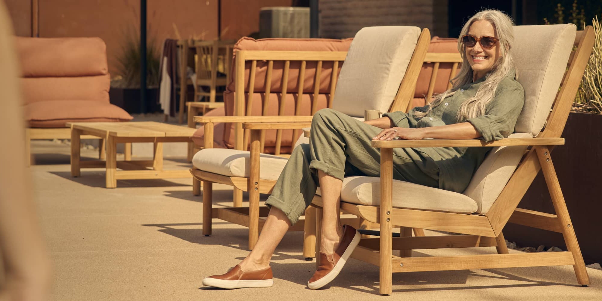 Woman comfortably sitting in cushioned teak deck chair in a modern backyard setting