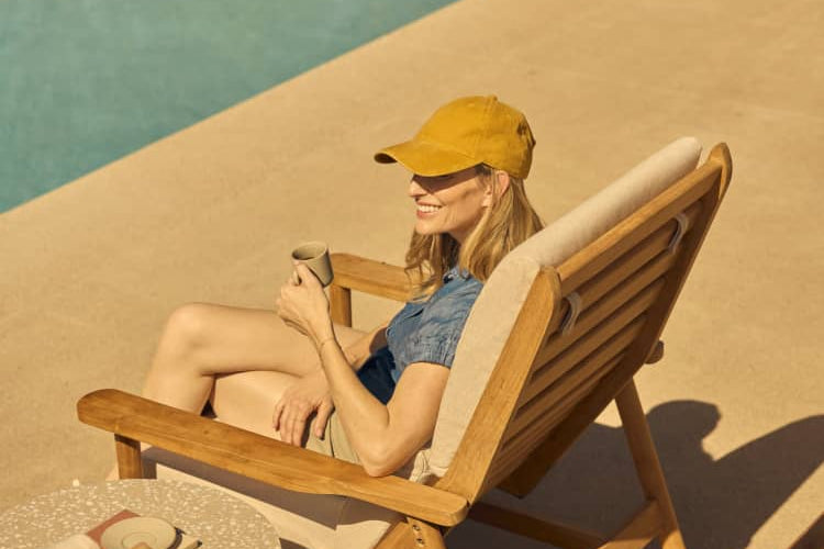 Rear view of a woman sitting in a teak deck chair across from a modern pool area.