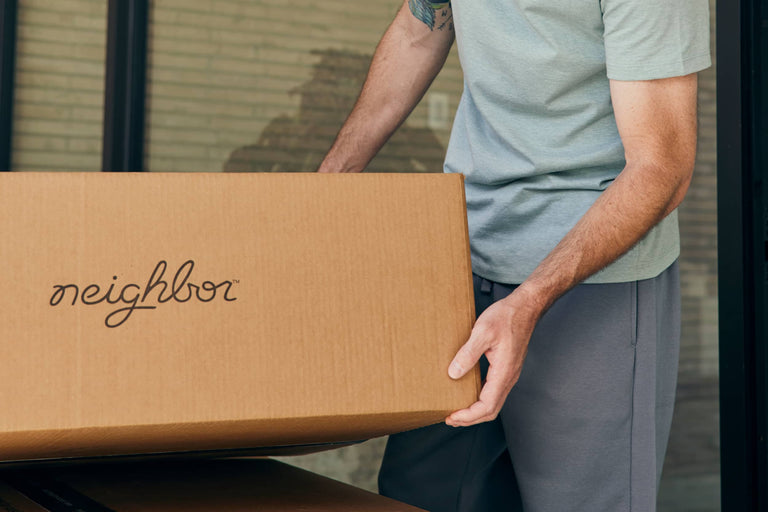Person carrying a Neighbor-branded cardboard box through a doorway