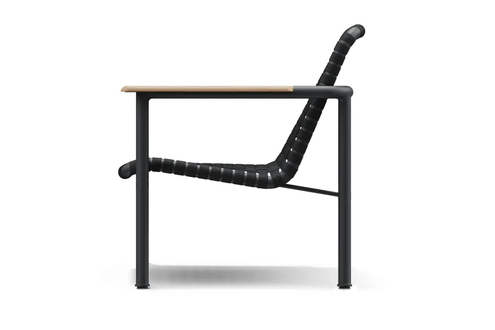 Studio side profile of a Neighbor Up-Down Chair on a clean white background, showing the curved charcoal woven-strap seat-and-back sling, natural-wood armrest, and black powder-coated tubular steel frame.