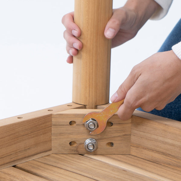 Hands assembling teak dining furniture, tightening a bolt at the table leg joint with a wrench