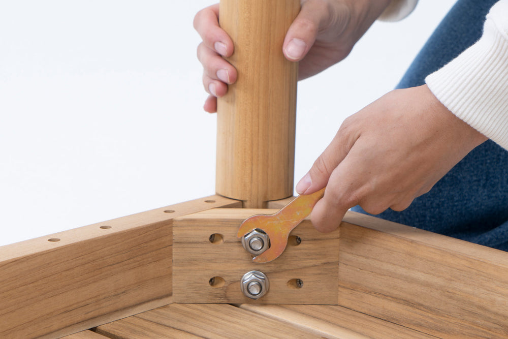 Hands assembling teak dining furniture, tightening a bolt at the table leg joint with a wrench