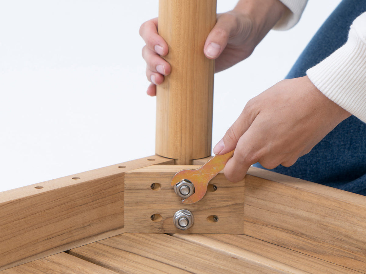 Hands assembling teak dining furniture, tightening a bolt at the table leg joint with a wrench
