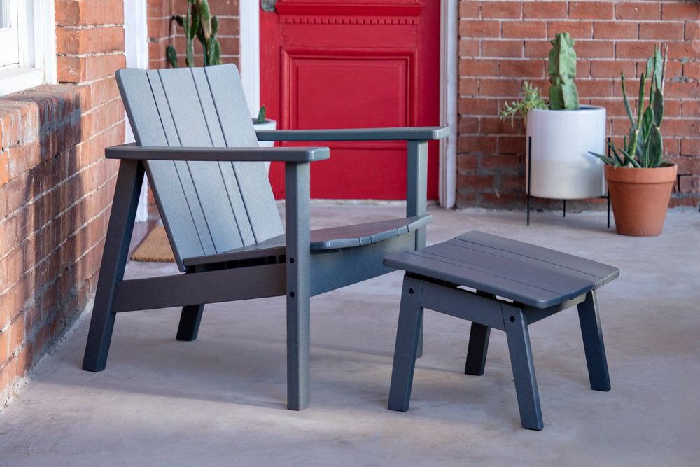 Neighbor Low Chair and Low Ottoman in charcoal polywood on a concrete front porch, red door and brick wall behind with cacti in planters