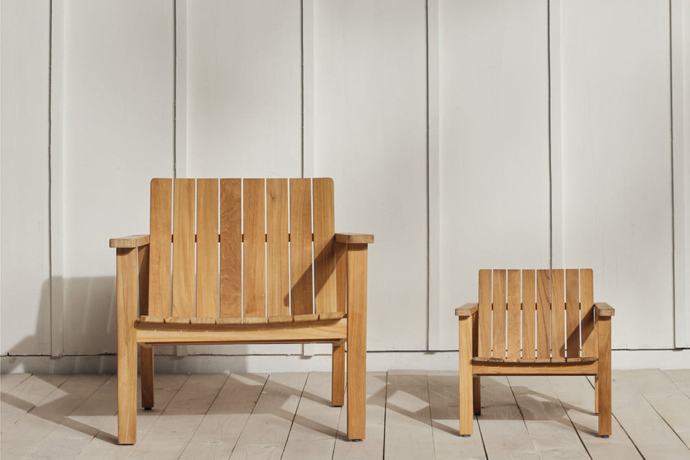 Full-size and child-size Neighbor Low Chairs in natural teak side by side against a white board-and-batten wall on a white-painted deck