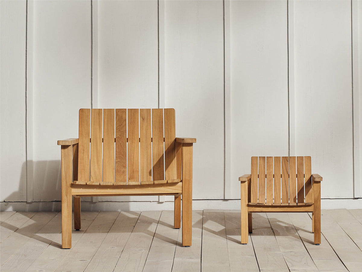 Full-size and child-size Neighbor Low Chairs in natural teak side by side against a white board-and-batten wall on a white-painted deck