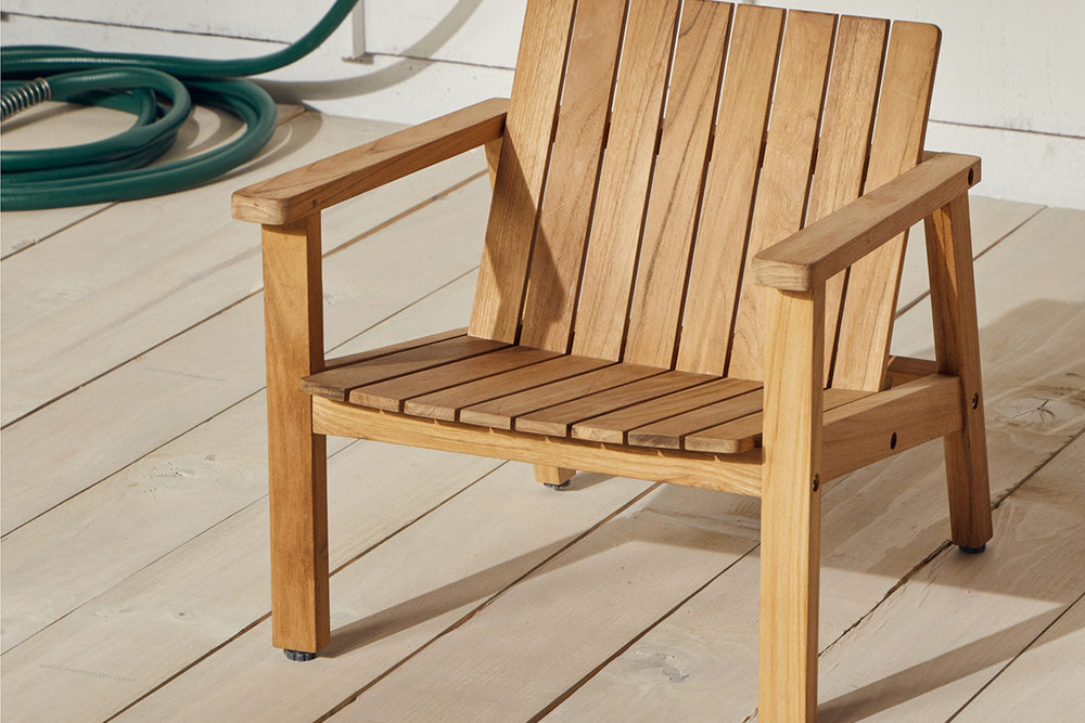 Child-size Neighbor Low Chair in natural teak on white deck boards, garden hose coiled in the background