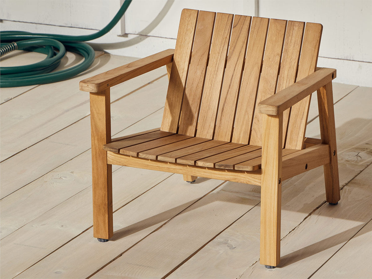 Child-size Neighbor Low Chair in natural teak on white deck boards, garden hose coiled in the background