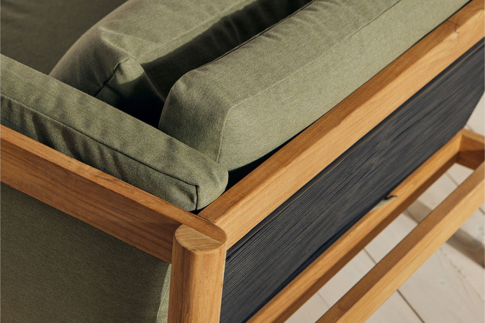 Close-up of teak chair arm and frame corner with sage green cushion, showing woven cord back panel and teak joinery