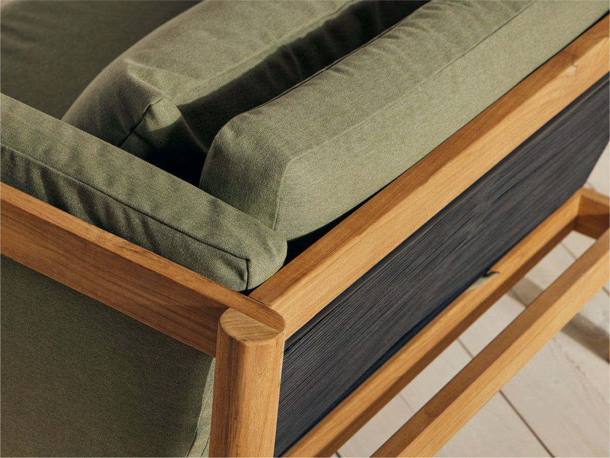 Close-up of teak chair arm and frame corner with sage green cushion, showing woven cord back panel and teak joinery