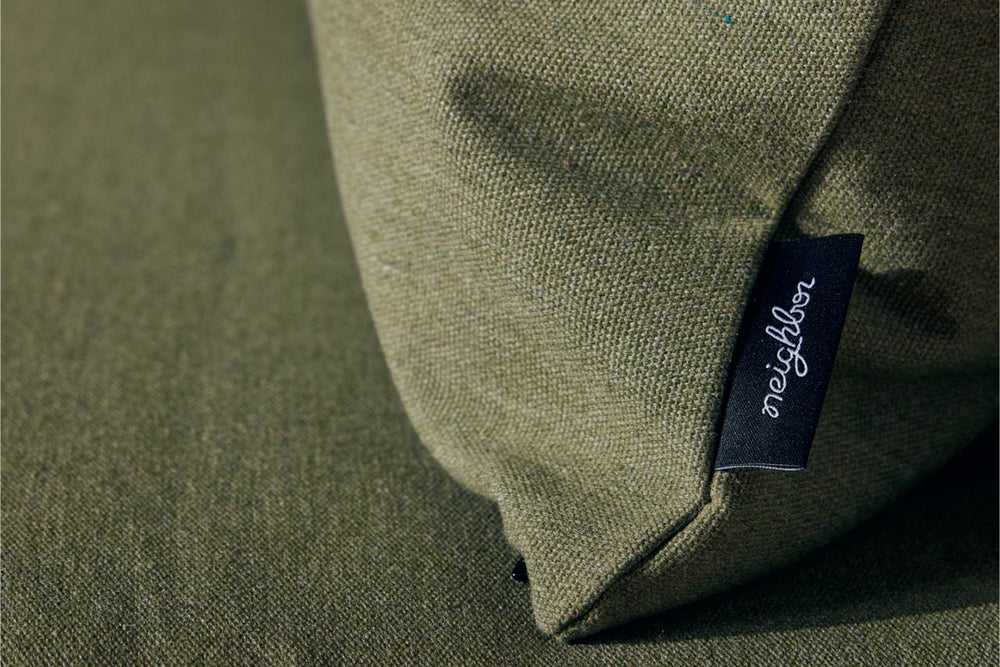 Close-up of sage green Neighbor outdoor cushion corner showing dark navy Neighbor brand label tag