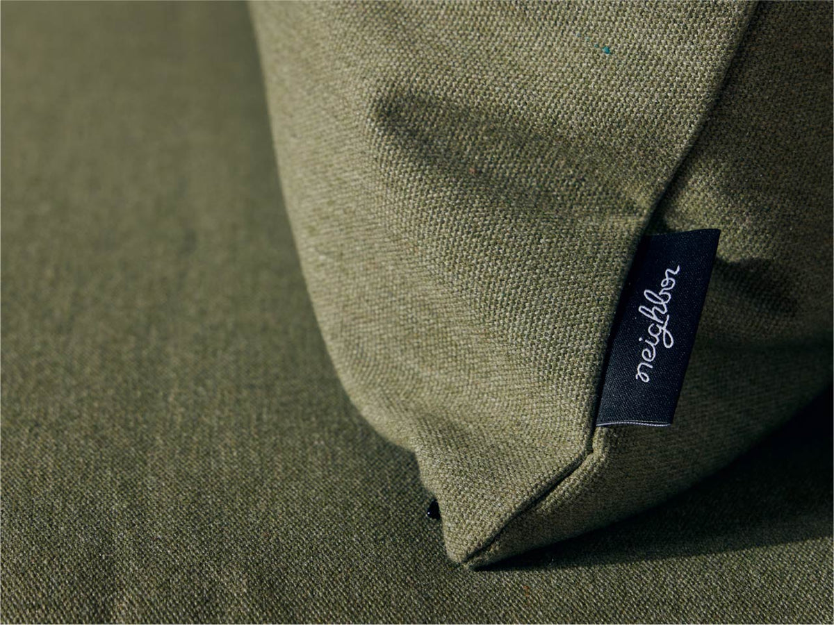 Close-up of sage green Neighbor outdoor cushion corner showing dark navy Neighbor brand label tag