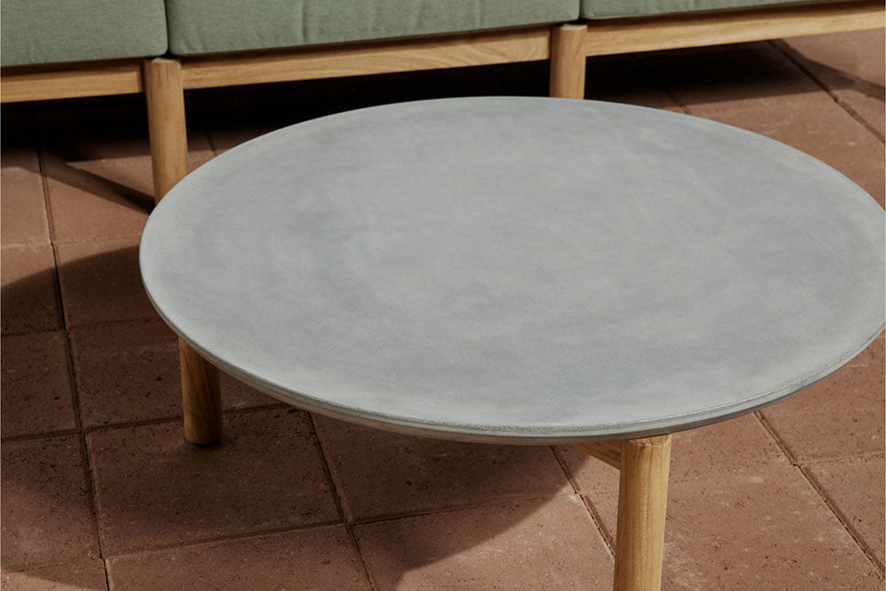Neighbor Haven Coffee Table with round concrete top and teak legs on terracotta tile, Haven Sectional cushions visible in background