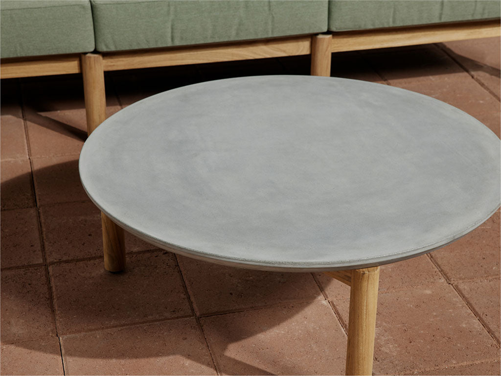Neighbor Haven Coffee Table with round concrete top and teak legs on terracotta tile, Haven Sectional cushions visible in background