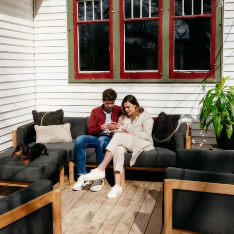 Customer photo - couple with newborn on Neighbor outdoor sectional in dark charcoal with teak frame on a wooden deck, dachshund beside them