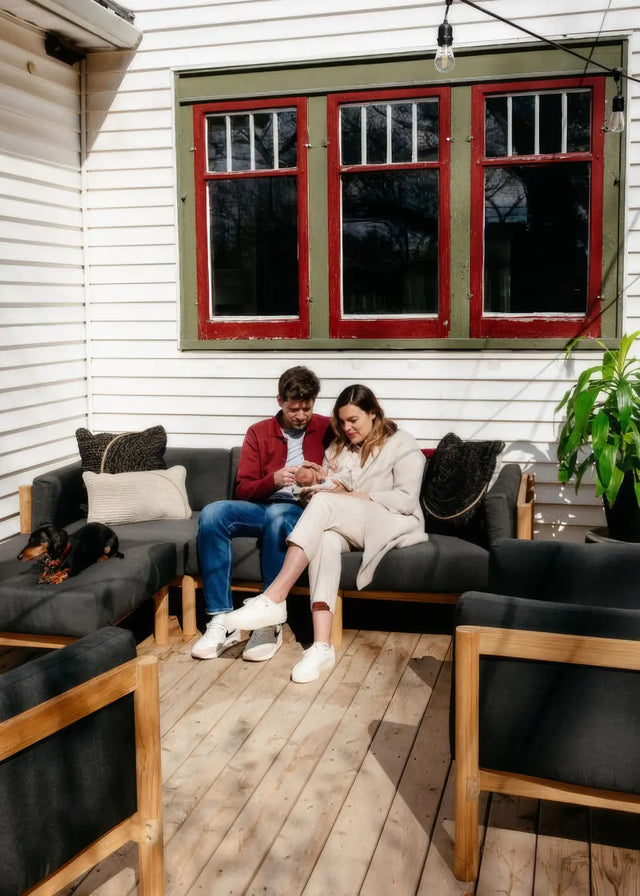 Customer photo - couple with newborn on Neighbor outdoor sectional in dark charcoal with teak frame on a wooden deck, dachshund beside them
