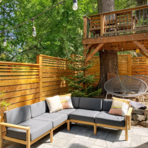 Customer photo - Neighbor outdoor sectional in dark charcoal on a stone patio with colorful throw pillows, string lights and treehouse behind